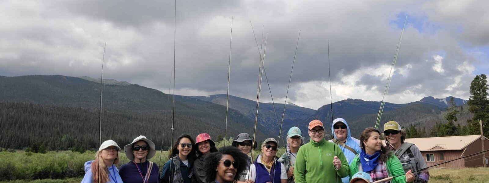 A group of women standing in front of mountains holding fly fishing poles.